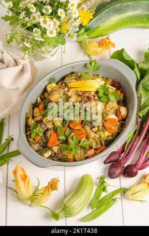 Cuire au four des légumes aux herbes dans un plat de cuisson sur fond de bois blanc Banque D'Images