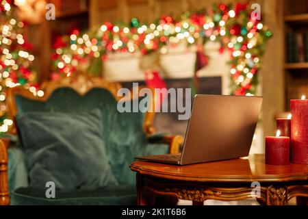 Image d'arrière-plan d'un ordinateur portable ouvert sur une table en bois avec des bougies dans le salon de fête décoré pour Noël, espace copie Banque D'Images