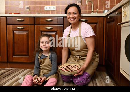 Charmante maman charmante et adorable petite fille tenant dans les mains tartes aux baies de cerises douces, souriant à l'appareil photo Banque D'Images