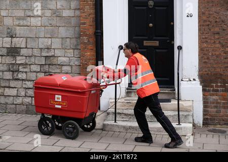 Le postier en blouson orange employé par le Royal Mail d'Angleterre pousse un grand chariot transportant le courrier dans les rues de Windsor, passant une porte d'entrée Banque D'Images