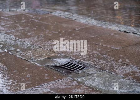 Chaussée humide en pierre avec anneaux concentriques de gouttes de pluie tombant et de l'eau s'écoulant dans une couverture de trou d'homme dans une rue. Surface de route humide dans un environnement urbain Banque D'Images