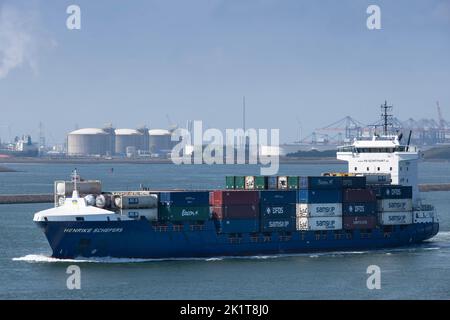 Un petit bateau à conteneurs quitte le port industriel de Hoek van Holland et navigue sur le 'Nieuwe Waterweg'. Grands réservoirs d'huile en béton en arrière-plan Banque D'Images
