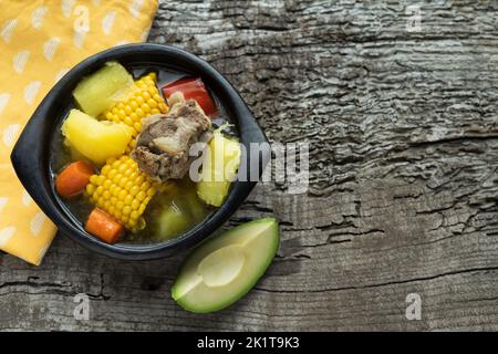 Sancocho, typical Colombian food in a black ceramic bowl on a rustic wooden background. Copy space. Top view. Banque D'Images