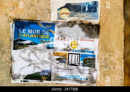 La Batterie des Arros au nord de Soulac-sur-Mer dans le Médoc, en France, porte sur l'une de ses parois de bunker un flyer de l'Association Historique de la Poche du Nord-Médoc (AHPNM) faisant la promotion de visites guidées sous le titre « Le Mur de l'Atlantique – La Batterie des Arros », avec les horaires d'ouverture, les tarifs d'entrée et un point de rendez-vous à la petite gare touristique dans le parking Les Arros à Soulac-sur-Mer. Un deuxième flyer partiellement délavé au-dessus porte le même logo de l'association. Le site fait partie des derniers survivants d'environ 350 bunkers constituant la « Festung Gironde-Süd » (forteresse du Sud de la Gironde) Banque D'Images