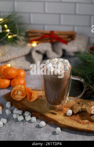 chocolat chaud dans une tasse en verre avec mini guimauves sur plaque en bois, arrière-plan de noël flou Banque D'Images