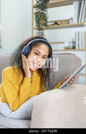 Un américain qui s'assoit sur un canapé avec une tablette et qui porte un casque pour se détendre Banque D'Images