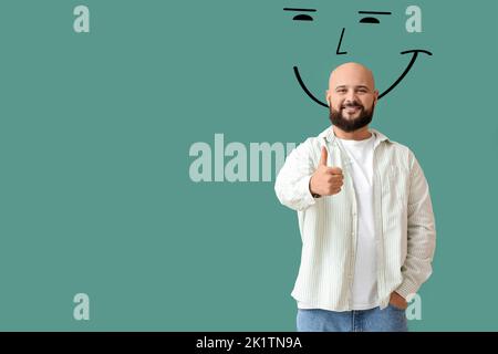 Un homme chauve heureux montrant le pouce vers le haut et souriant sur fond vert Banque D'Images