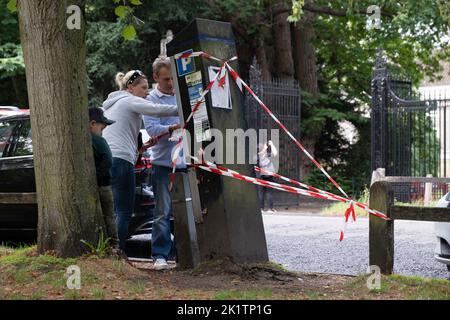 Couple avec des béquilles pour enfants devant une machine de stationnement torchée qui est protégée contre la chute par des rubans rouges et blancs. Une voiture l'a frappé Banque D'Images