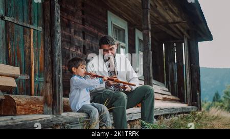 Petit garçon avec papa jouant sur des flûtes en bois de vent - sopilka ukrainien. Duet familial, concept de musique folk. Père et fils brodés traditionnels Banque D'Images