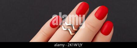 Gros plan de la main des femmes avec des ongles rouges mat sur fond noir. Manucure, pédicure tendances design Banque D'Images