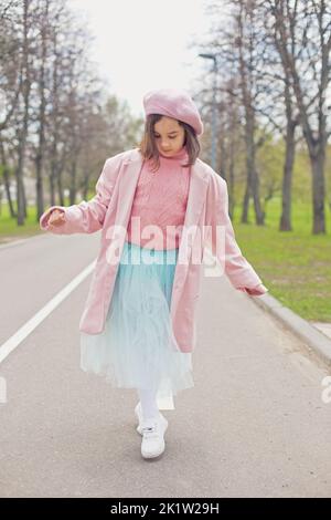 une petite fille charmante marche le long d'une route asphaltée dans le parc de printemps. Banque D'Images