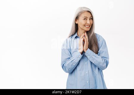Souriante vieille femme asiatique, femme âgée scheming, a le plan, la pensée de quelque chose avec la ruse, le sourire coï, les doigts steeple, debout sur blanc Banque D'Images