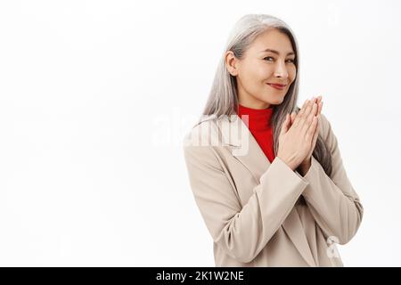 Portrait d'une femme asiatique âgée souriante, femme d'affaires se frottant les mains avec une expression du visage satisfaite, debout sur fond blanc Banque D'Images