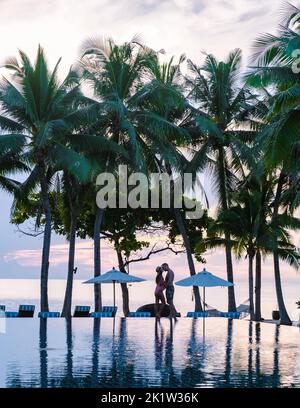 Deux hommes et femmes se détendent au bord de la piscine dans des chaises de plage, une piscine tropicale et une piscine avec des palmiers à la plage donnant sur l'océan Banque D'Images