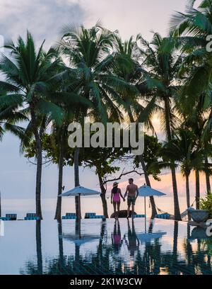 Deux hommes et femmes se détendent au bord de la piscine dans des chaises de plage, une piscine tropicale et une piscine avec des palmiers à la plage donnant sur l'océan Banque D'Images