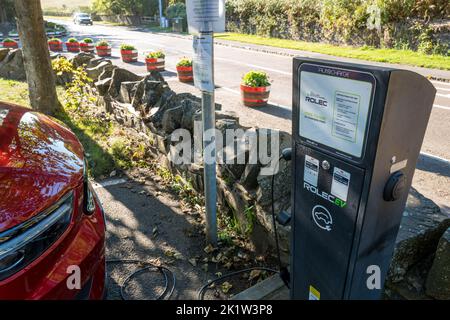 Voiture électrique branchée dans un point de recharge libre de Rolec dans un parking du village de pêcheurs de Craster, Northumberland, Angleterre. Banque D'Images