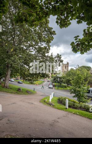 La route principale bordée d'arbres traverse la petite ville marchande de Rothbury, dans le Northumberland, en Angleterre, avec l'église All Saints en arrière-plan. Banque D'Images