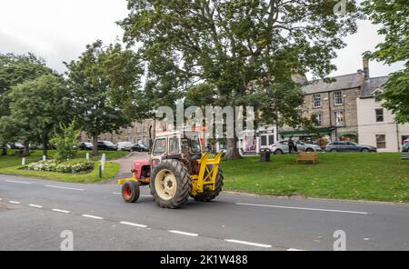 Tracteur d'époque descendant la route principale bordée d'arbres à travers la petite ville marchande de Rothbury, à Northumberland, en Angleterre. Banque D'Images