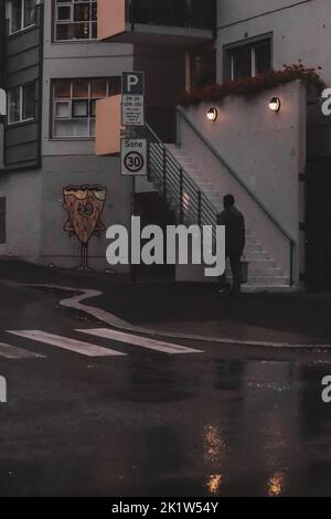 Un homme en blouson noir marchant devant un escalier et un graffiti sous la pluie Banque D'Images