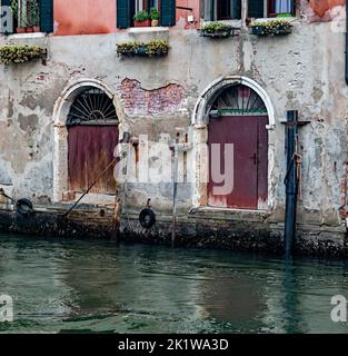 Gros plan de l'ancienne façade d'un vieux bâtiment coloré avec portes et fenêtres sur un canal avec réflexion d'eau à Venise, Italie. Banque D'Images