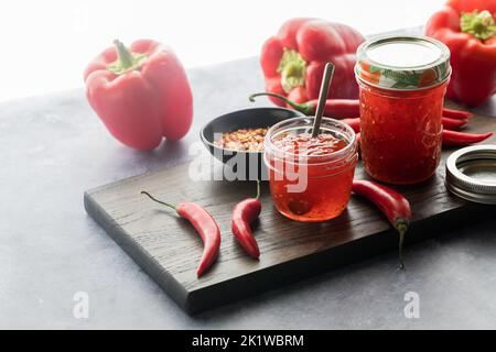 Des bocaux de gelée de poivron rouge délicieux contre une fenêtre ensoleillée. Banque D'Images