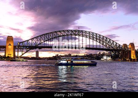 A Manly Fast Ferry passing in front of the Sydney Harbour Bridge at dusk Stock Photo