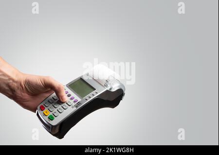 Cash terminal dans la main d'un homme sur un fond gris clair. Minimalisme. Ventes, achats, achats en ligne, vente au détail et en gros, cartes bancaires et cartes de crédit. B Banque D'Images