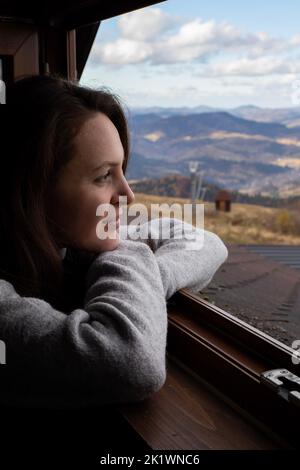 Jeune femme assise dans une maison confortable et regardant le fond des montagnes Banque D'Images
