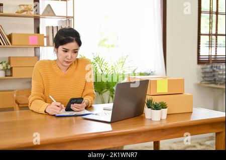 Une jeune femme asiatique d'affaires ou propriétaire de petite entreprise en ligne a concentré son travail sur son entreprise, en vérifiant la commande sur ordinateur portable. Banque D'Images