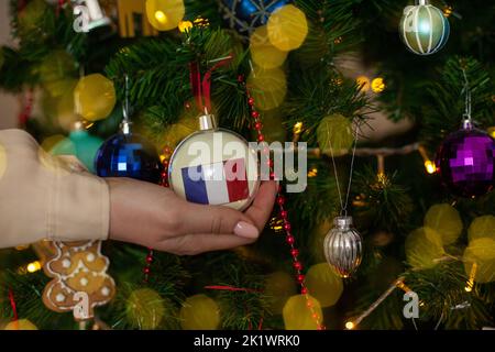 Gros plan de filles main tenant une boule de Noël pour un sapin avec le drapeau de la France. Nouvelle année en France. Carte de vœux de Noël avec copie Banque D'Images