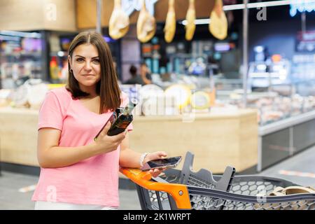 Une jeune belle femme tient une bouteille d'huile dans sa main et prend une photo d'elle sur un téléphone portable. Dans les étagères d'arrière-plan avec les produits. Le c Banque D'Images