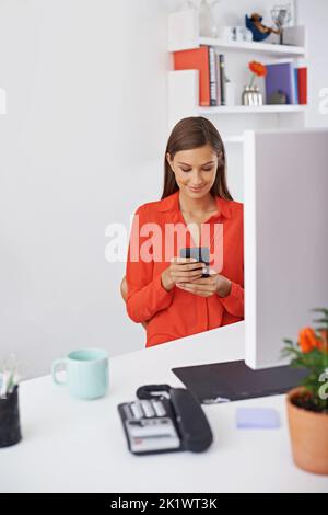 Prenez un moment pour rester connecté. Une jeune femme au bureau tout en utilisant son téléphone Banque D'Images