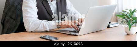 L'homme caucasien est assis à une table près d'un ordinateur portable dans le bureau et regarde l'écran. Un patron ou un employé sérieux et réfléchi travaillant sur son lieu de travail et se sentant intéressé ou analysant les résultats. Banque D'Images
