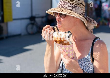 Belle femme portant des lunettes de soleil et chapeau de paille, dans une robe d'été légère, manger de la crème glacée sur une gaufre bulle dans la rue. Vacances d'été Banque D'Images