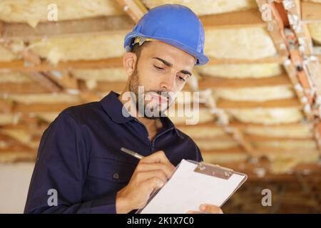 Homme builder ou d'ouvrier en casque writing on clipboard Banque D'Images