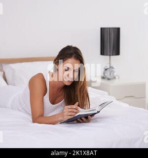 Vraiment entrer dans ce roman... une belle jeune femme lisant un livre tout en étant couché sur son lit. Banque D'Images