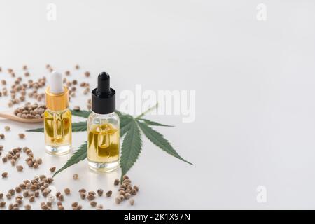 Caractéristiques du concept de marijuana légalisée avec extrait d'huile de CBD de marihuana en bouteille de verre avec couvercle compte-gouttes, piles de graines de chanvre sur fond vide Banque D'Images