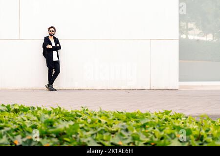 jeune homme avec des lunettes de soleil penchées dans un mur blanc Banque D'Images