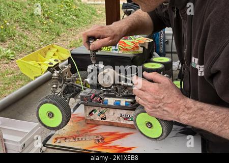 man working on the radio controlled buggy car model, internal combustion engine, during the regional championship scale 1/8 off road in dirt track Il Stock Photo