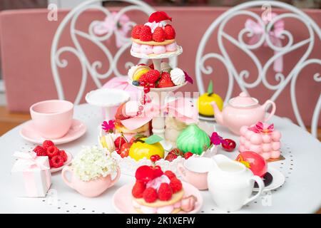 Assortiment abondant de desserts au sucre avec boîte et théière sur table blanche avec chaises dans le café ou le restaurant Banque D'Images