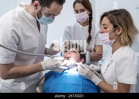 Dentiste de sexe masculin avec des assistants examinant les dents de garçon dans le fauteuil du dentiste. Clinique dentaire Banque D'Images