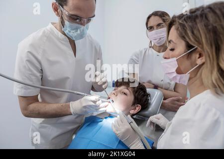 Dentiste de sexe masculin avec des assistants examinant les dents de garçon dans le fauteuil du dentiste. Clinique dentaire Banque D'Images