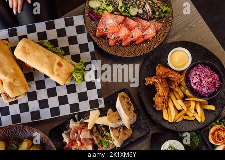 Déjeuner complexe au restaurant. Délicieux sandwich sur serviette à carreaux, salade de poisson, légumes, ciabatta, poulet, fromage sur assiette Banque D'Images