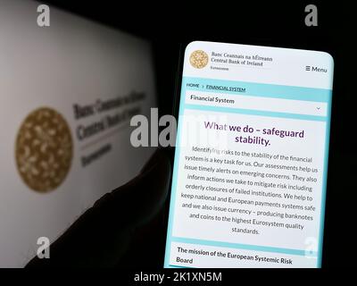 Person holding cellphone with webpage of financial institution Central Bank of Ireland on screen with logo. Focus on center of phone display. Stock Photo