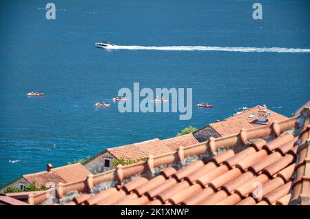 Groupe de bateaux avec rameurs, un hors-bord faisant une trace et avec un détail des toits rouges dans un village côtier Banque D'Images