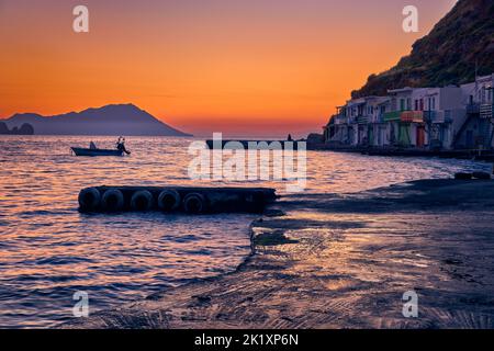 Coucher de soleil dans le village de pêcheurs de Klima, île de Milos, Grèce. Adulte simple, profitez d'une vue sur le coucher du soleil sur la jetée du petit village de pêcheurs, les collines brumeuses et le petit bateau. Banque D'Images