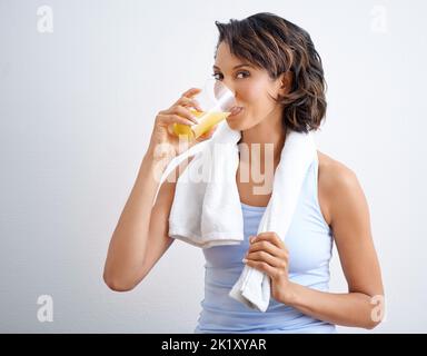 Boire un verre après une séance de remise en forme. Une belle jeune femme qui profite d'un verre de jus d'orange frais. Banque D'Images