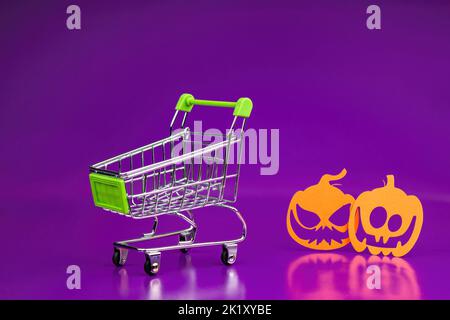 deux citrouilles en colère coupées en carton orange regardent un panier sur un fond violet Banque D'Images