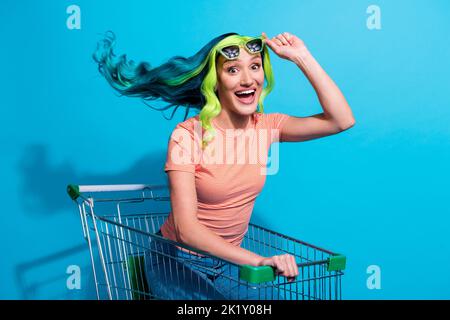 Photo de la jeune femme charmante avec des cheveux turquoise vif ont plaisir à monter dans le panier isolé sur fond bleu de couleur Banque D'Images