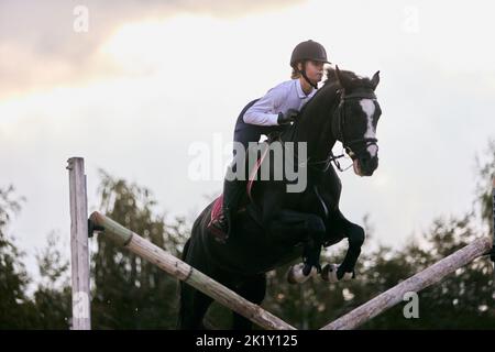 Sautez sur la barrière. Jeune fille sportive, entraînement des adolescents à l'arène d'équitation en été, en plein air. Dressage de chevaux. Équitation. Modèle dans le sport Banque D'Images